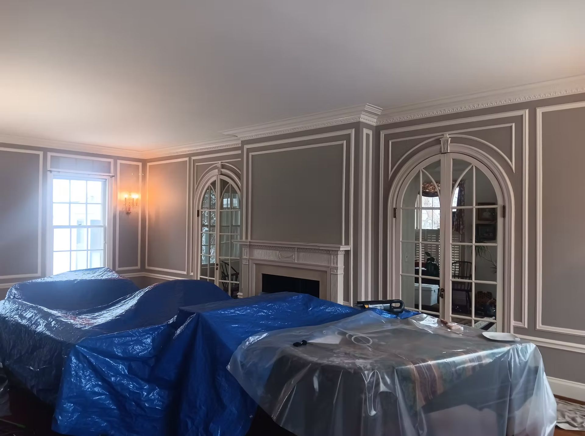 Room with gray walls, white trim, arched doors, and furniture covered in blue tarps.