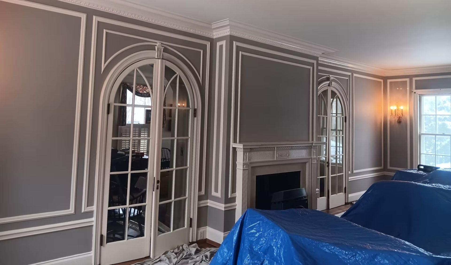 Elegant room with arched doorways, fireplace, and white trim against gray walls. Blue tarps cover furniture.