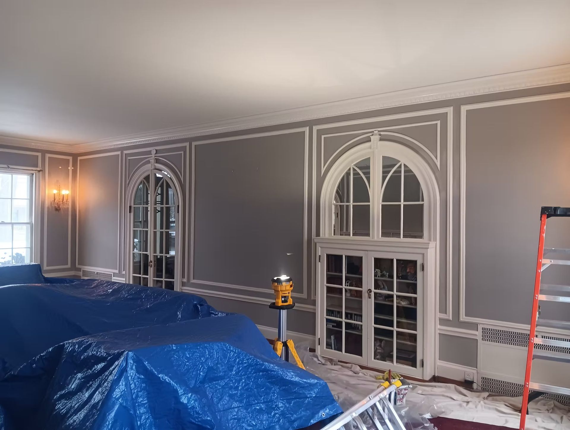 Interior room with gray walls, white trim, and arched windows. Blue tarps cover furniture.