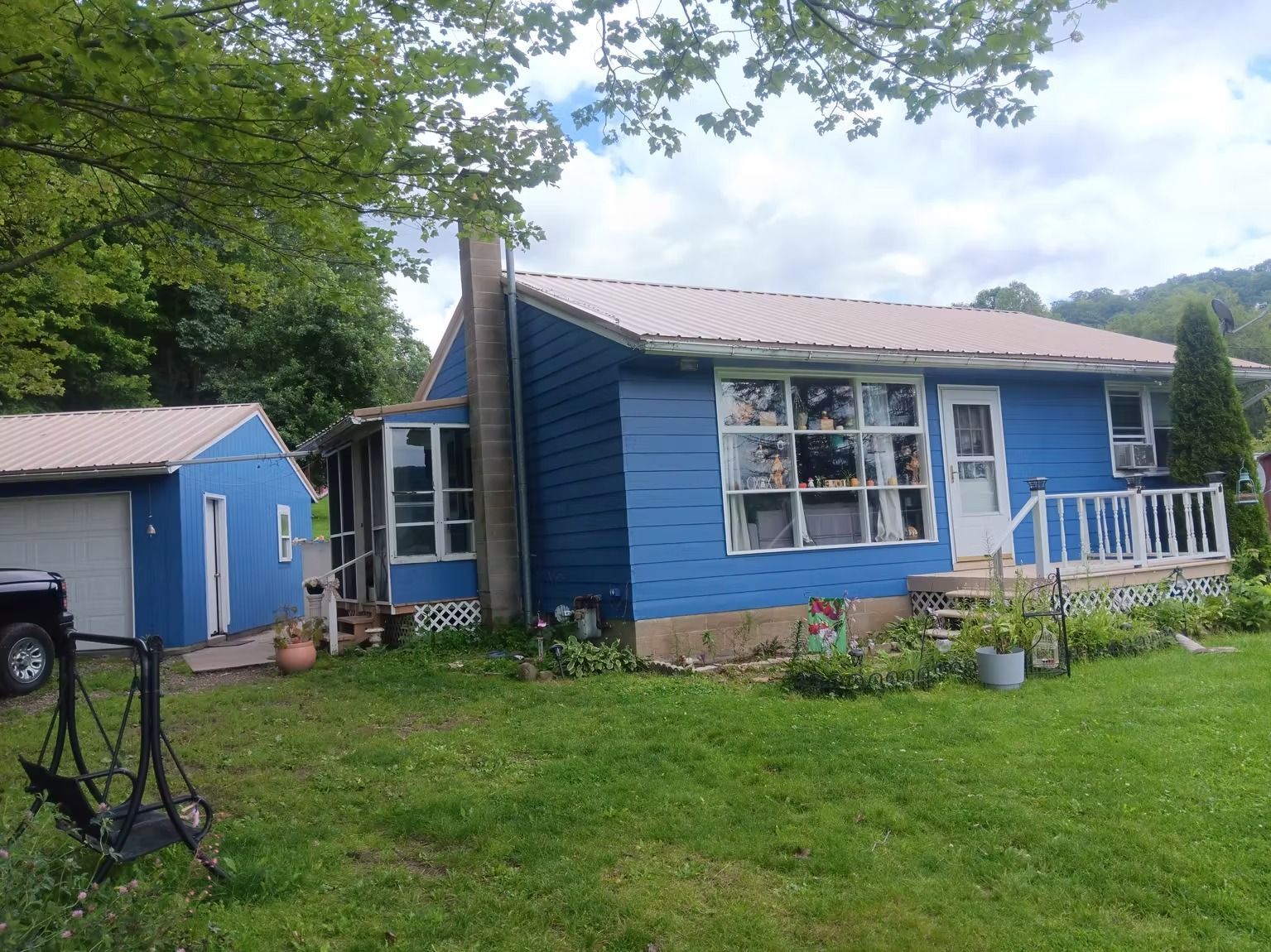 Blue house with a metal roof, chimney, and attached garage on a grassy lot.
