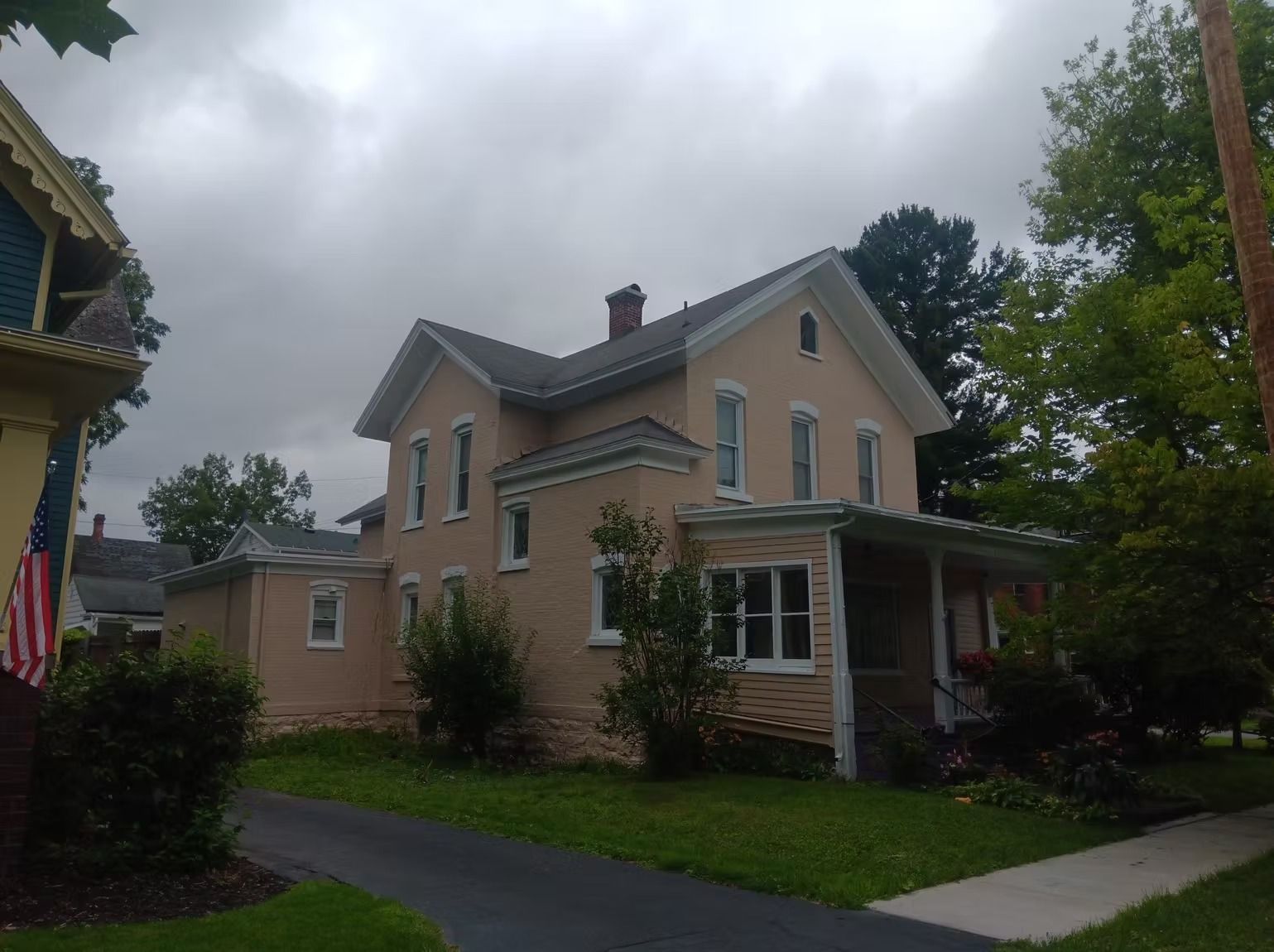 Two-story tan house with a porch and dark driveway on a cloudy day.