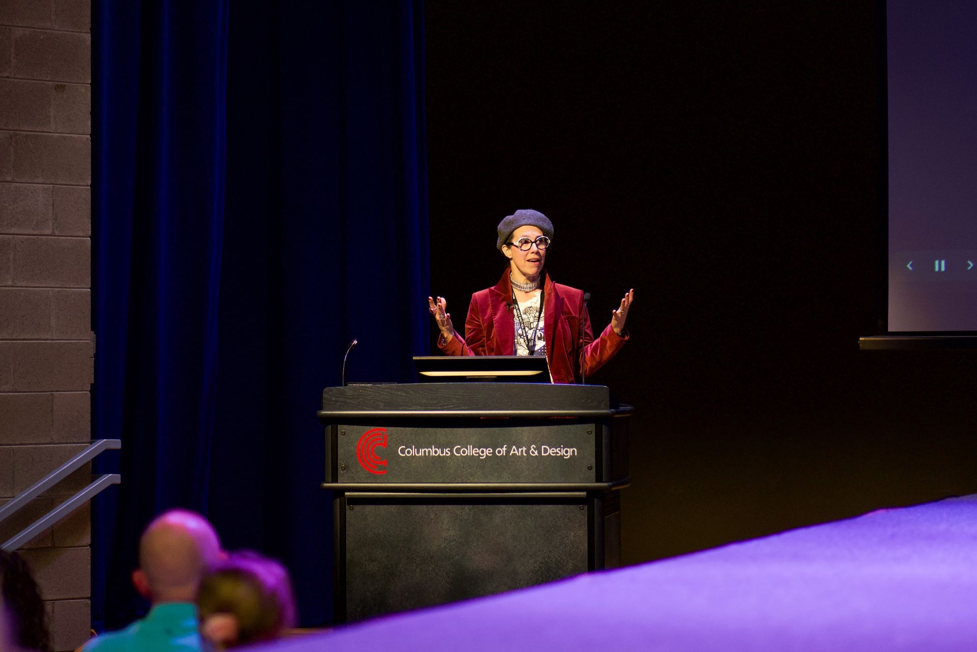 Priscilla is standing at a podium on a CCAD Stage giving a presentation to a group of people.