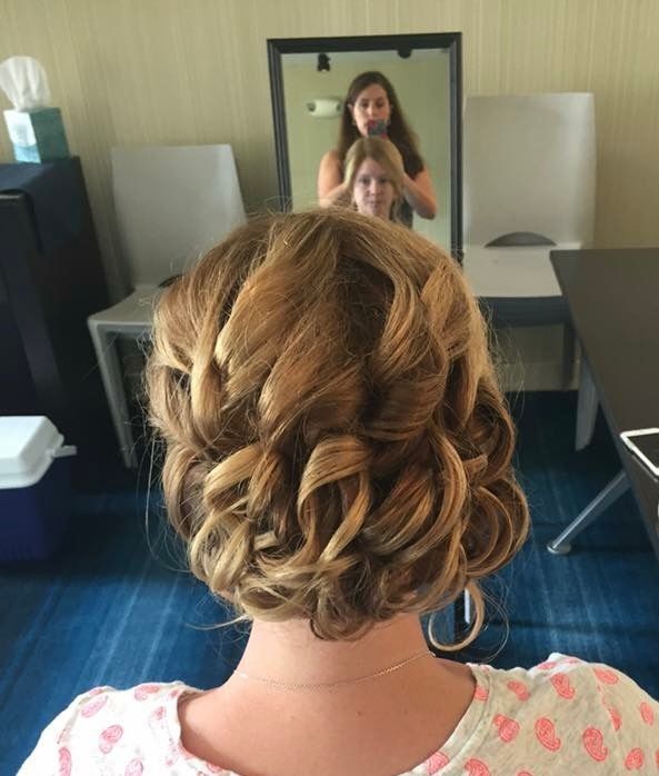 Woman getting her hair styled, brown curls in updo, indoors with mirror reflection.
