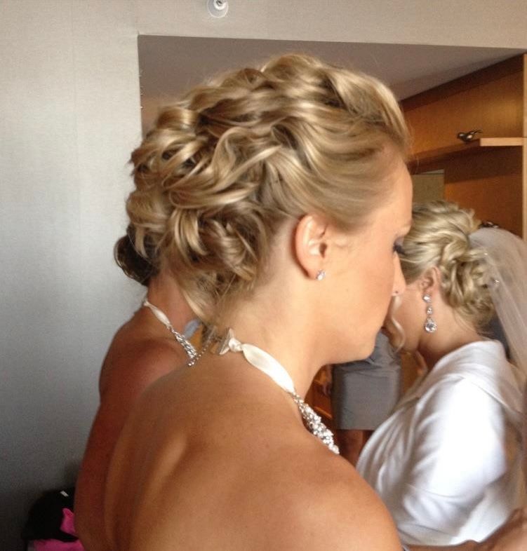 Blonde woman with curled updo hairstyle, wearing a white dress, possibly a bride getting ready.