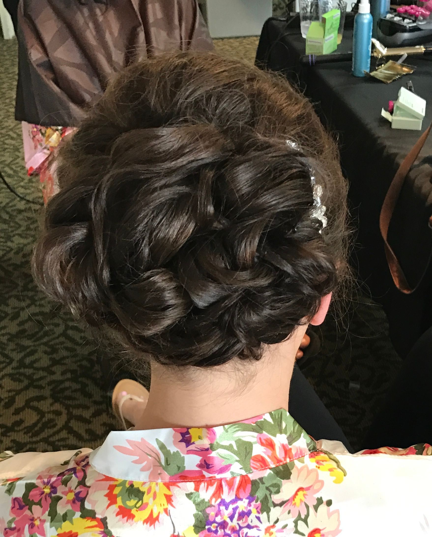 Person with dark brown hair in an updo; wearing a floral robe, sitting at a table in a brightly lit setting.