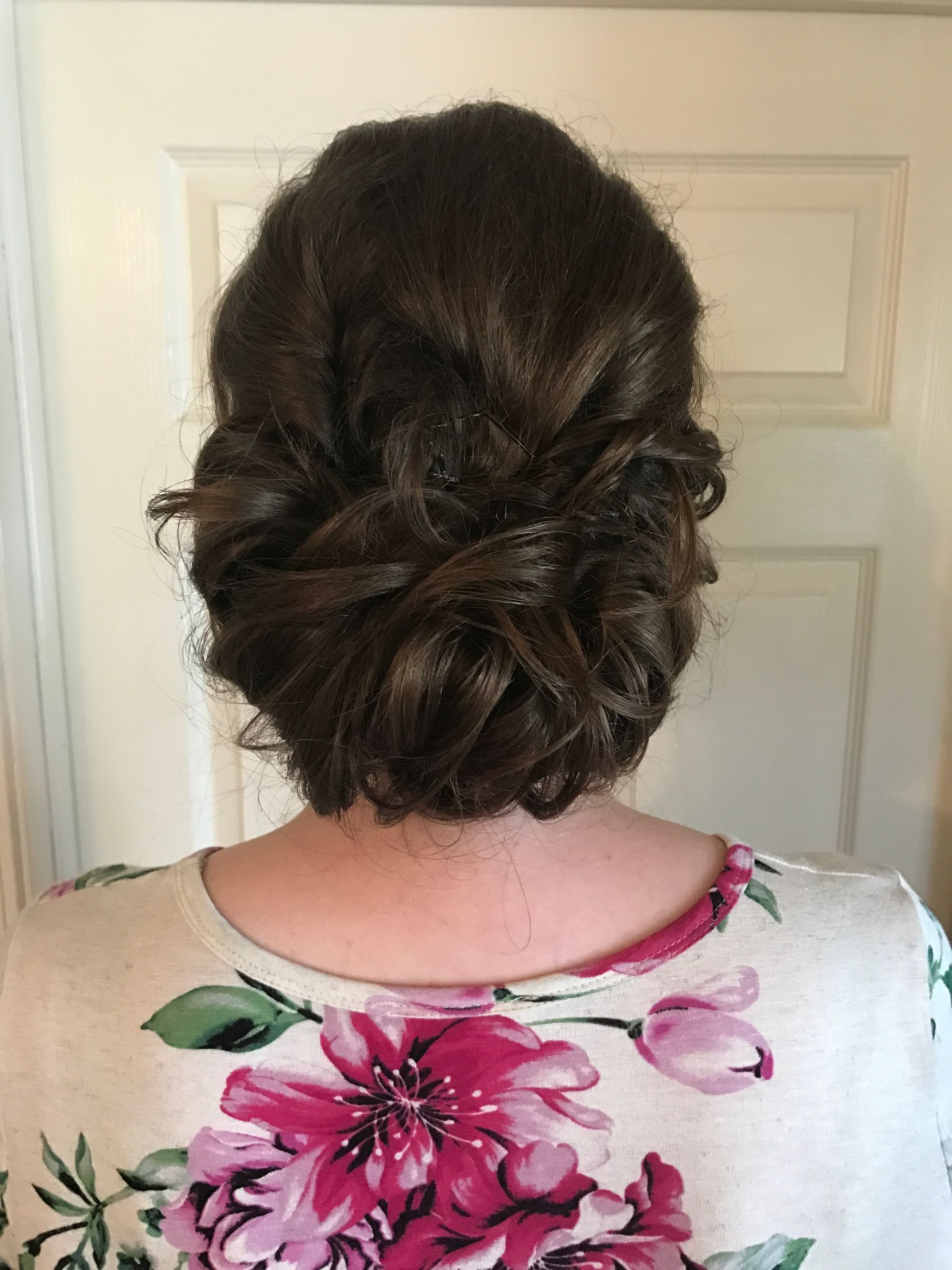 Woman's dark brown hair in an updo, showcasing a twisted bun style. She wears a floral print top.
