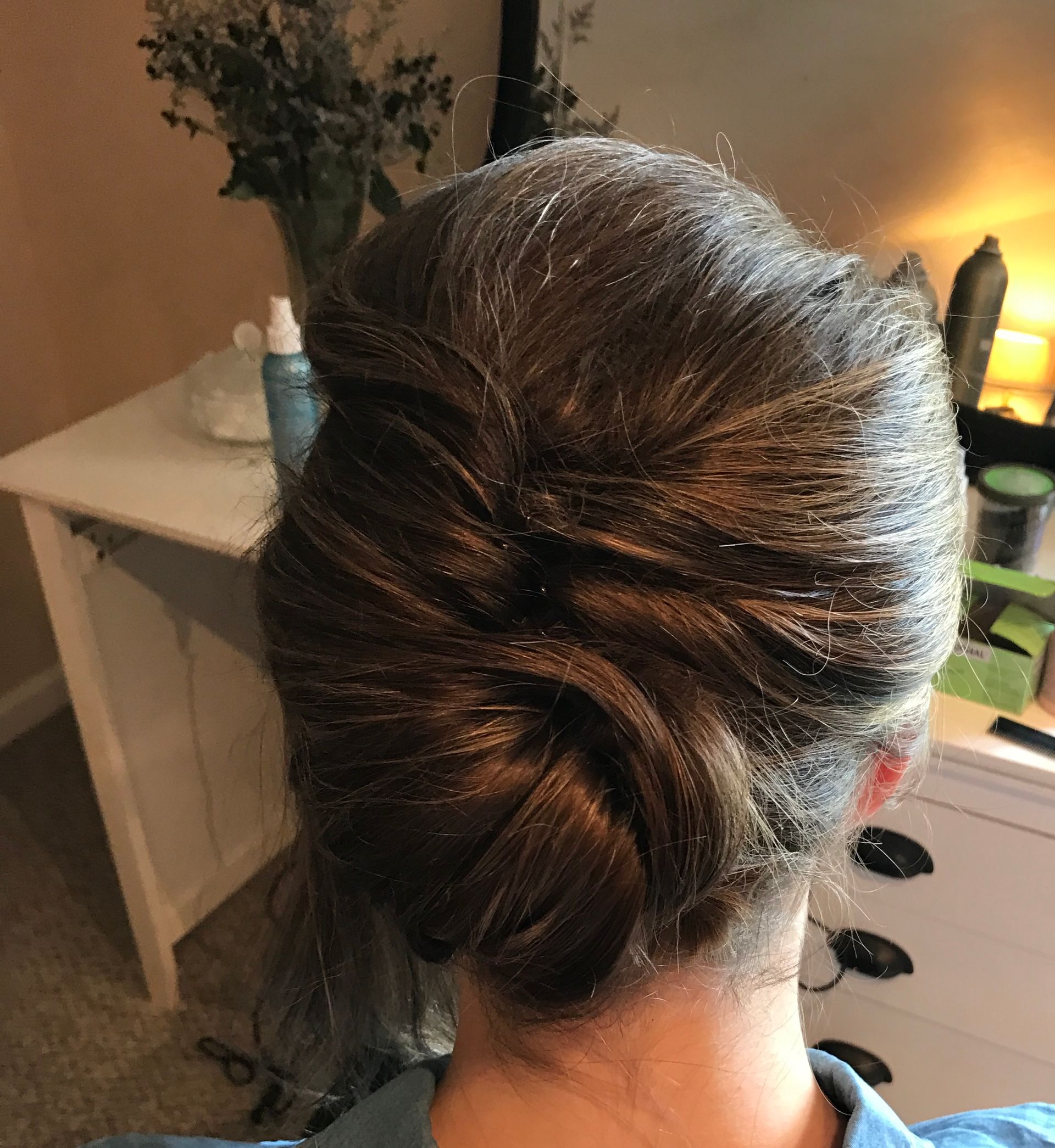 Woman with brown hair in an updo, back view. Hair has light reflective material and is styled with twists and a low bun.