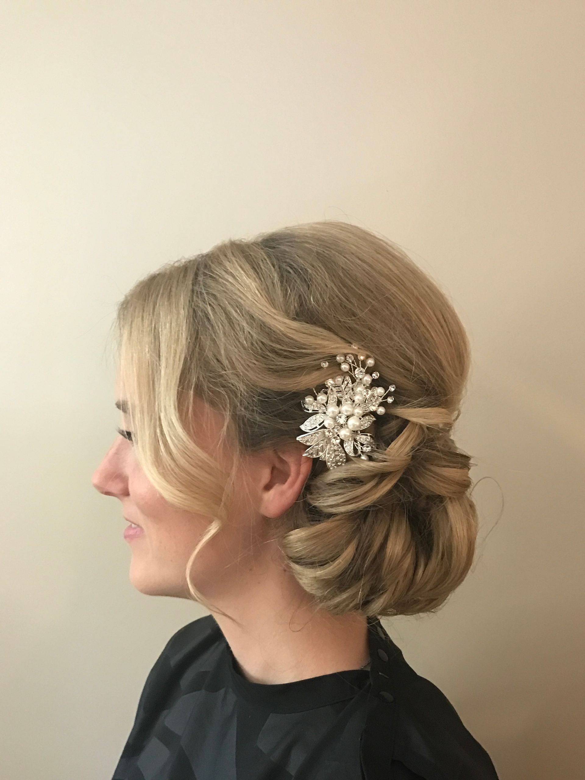 Woman with blonde hair styled in an updo, wearing a decorative hair clip, smiling.