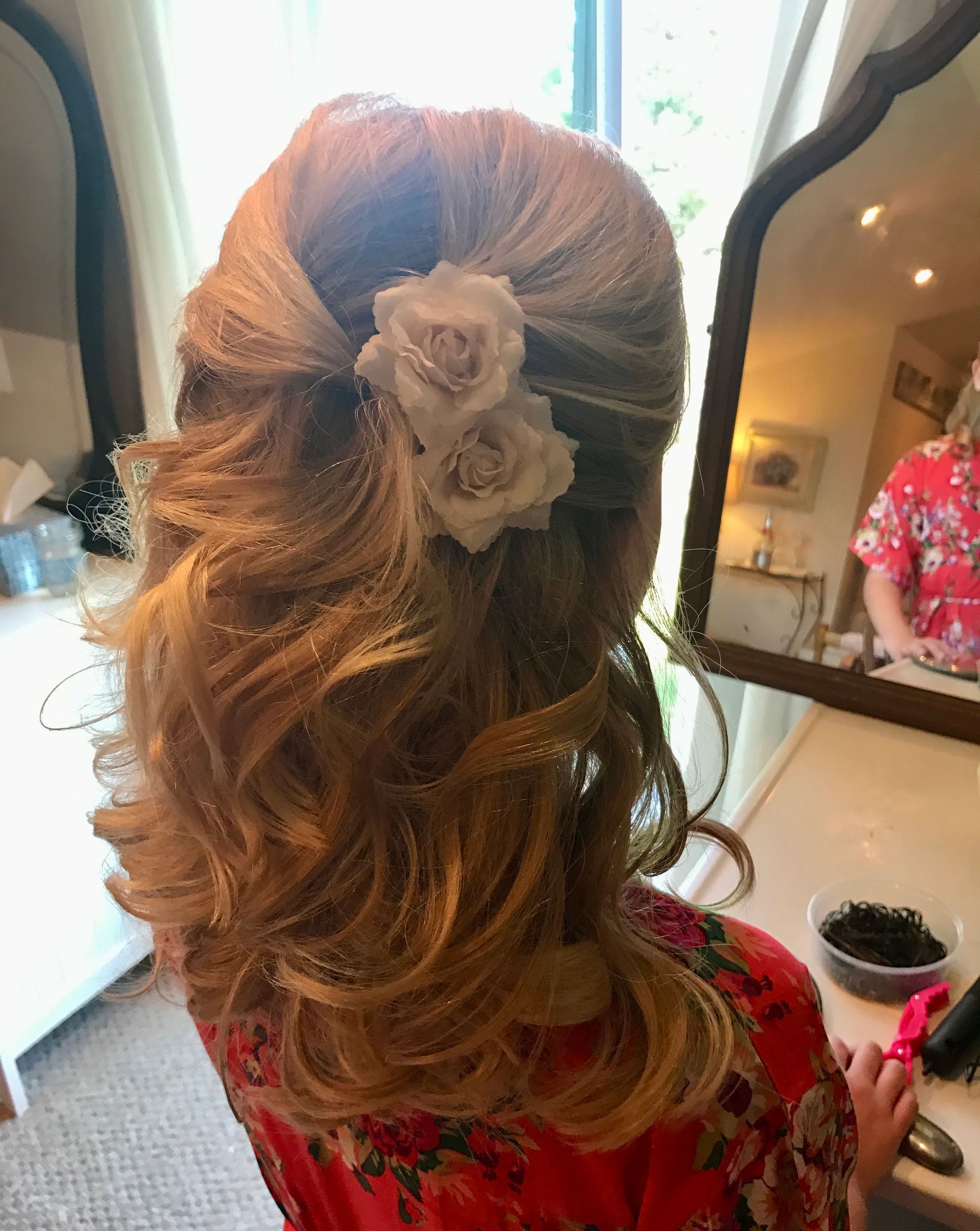 Woman with curled blonde hair in a half-up style, adorned with two white fabric roses.