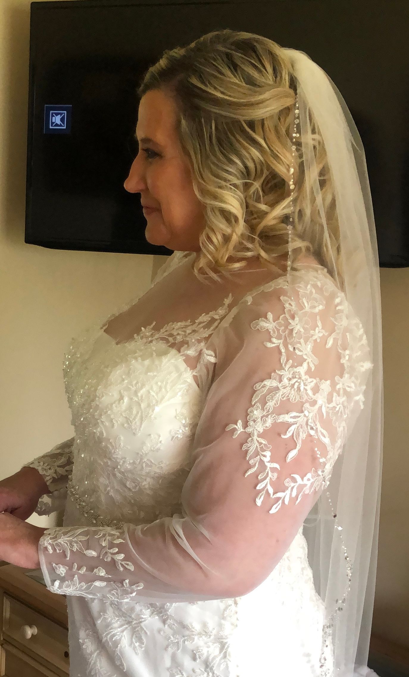 Woman in a white wedding dress with lace sleeves and a veil, posing indoors.
