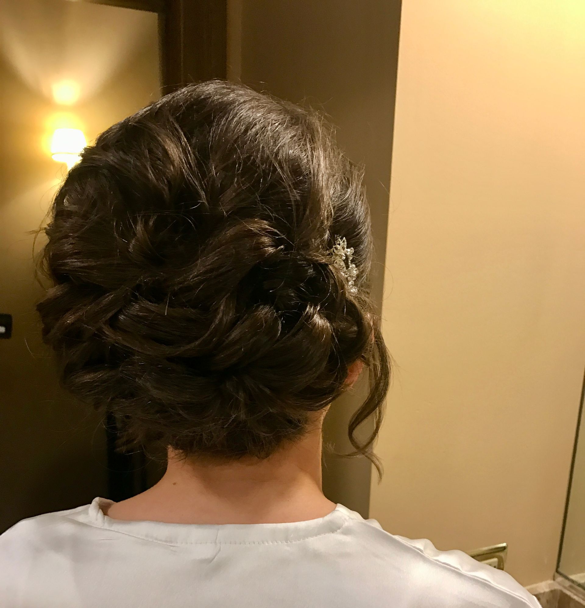 Woman with dark hair styled in an updo, with a hair accessory and a white top.