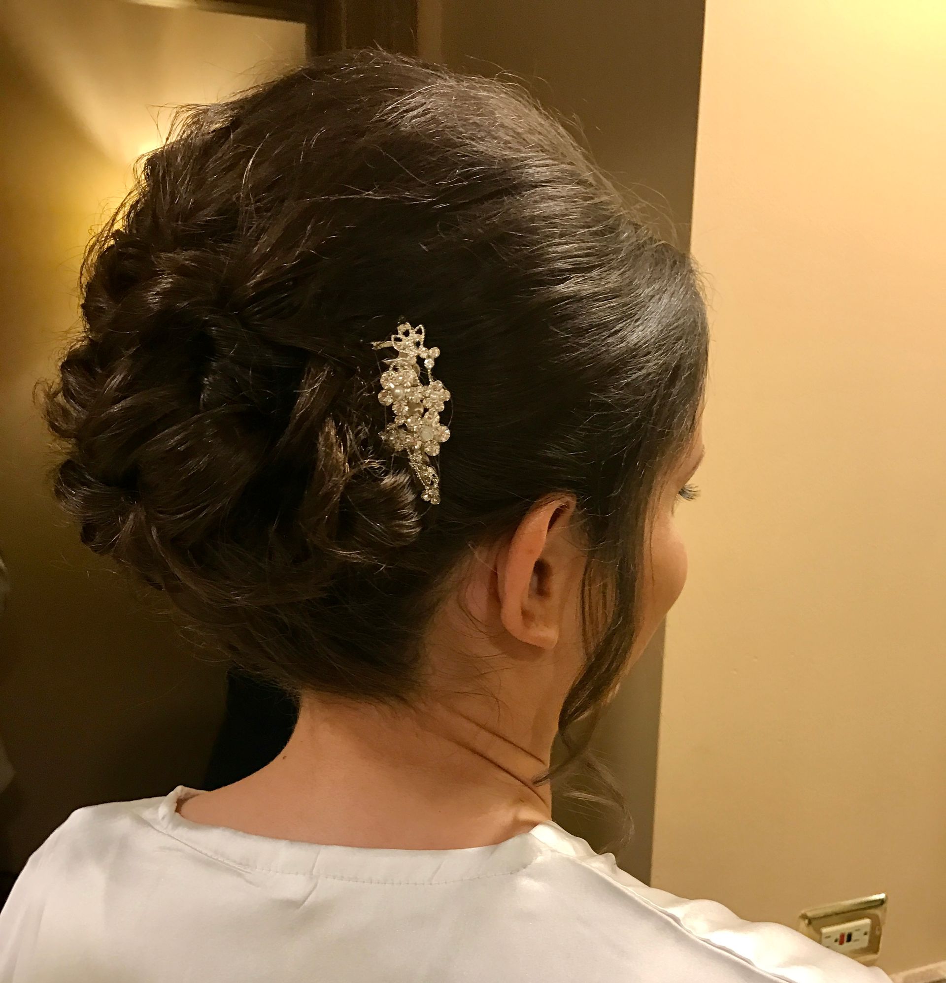 Woman with dark hair updo, pearl hairpiece, white top, indoors.