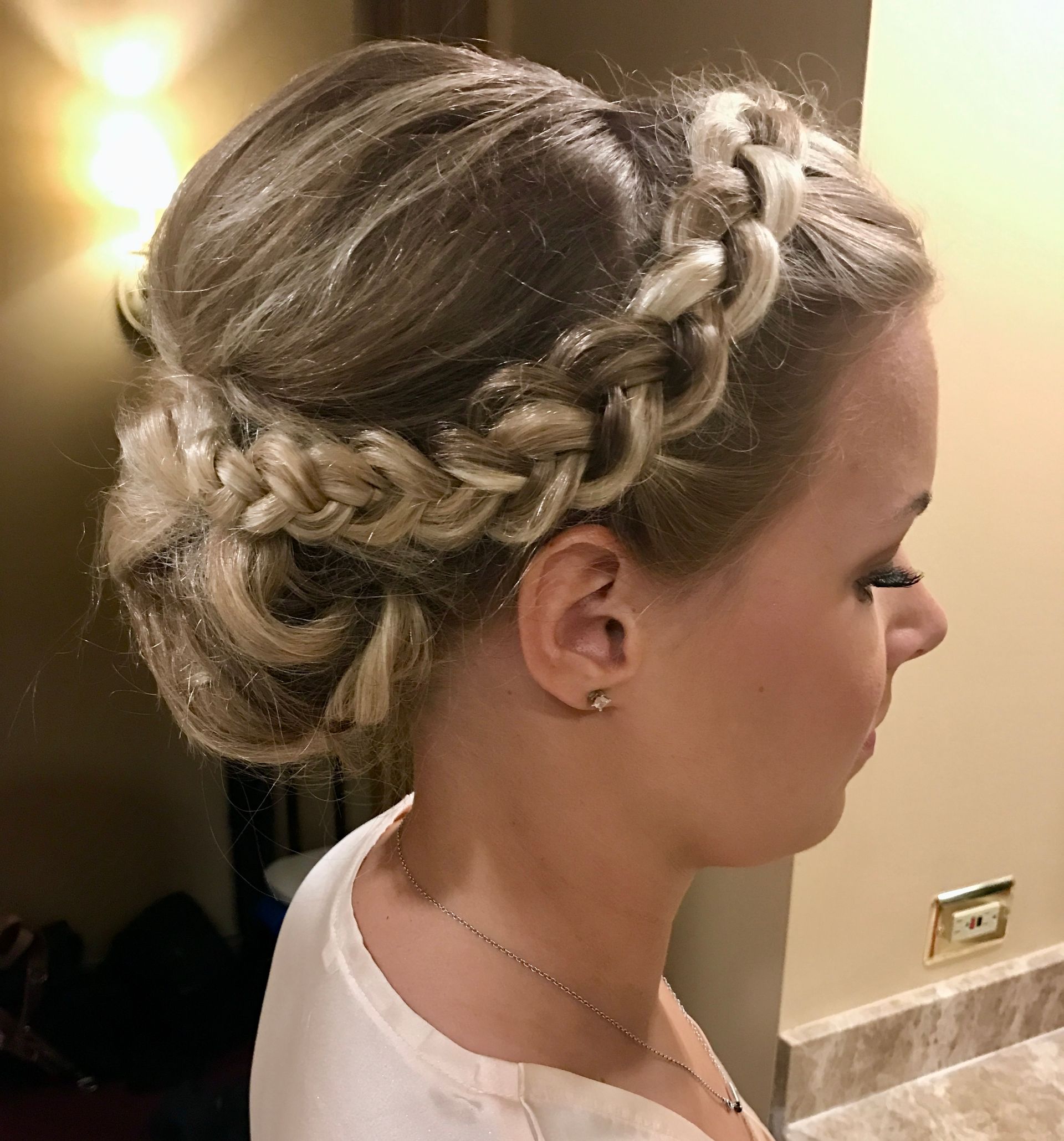 Woman with blonde hair styled in a braided updo, wearing a white shirt, turned to the side.