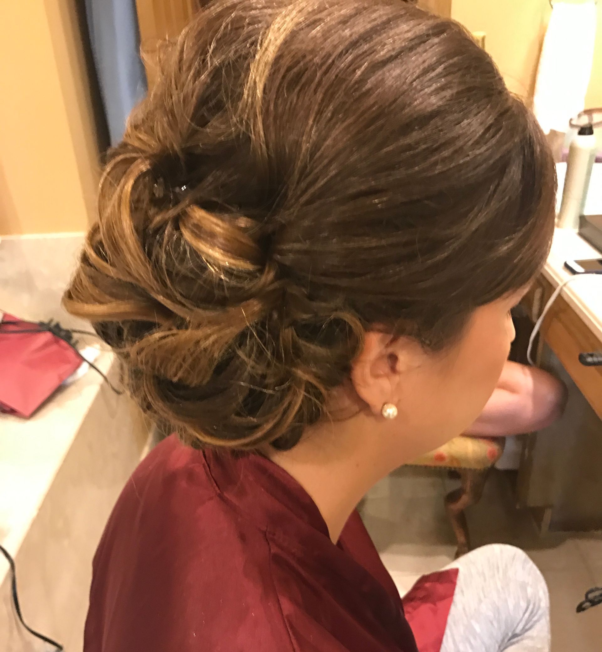 Woman with brown updo hairstyle, wearing a maroon robe and pearl earrings.