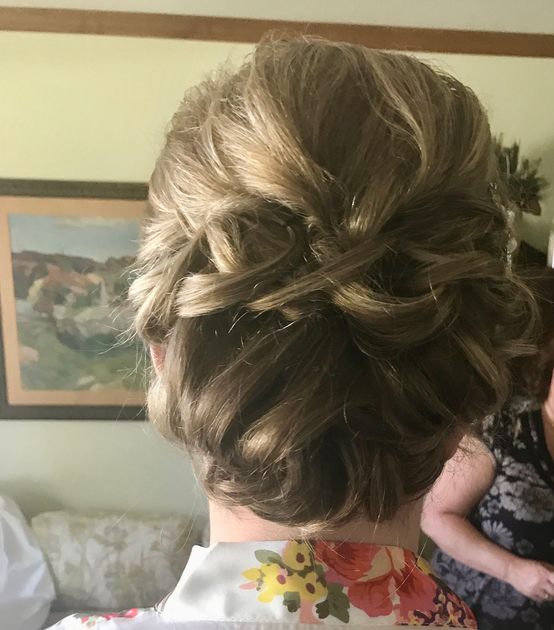 Woman with a light brown updo hairstyle; soft curls and interwoven sections, floral robe visible.