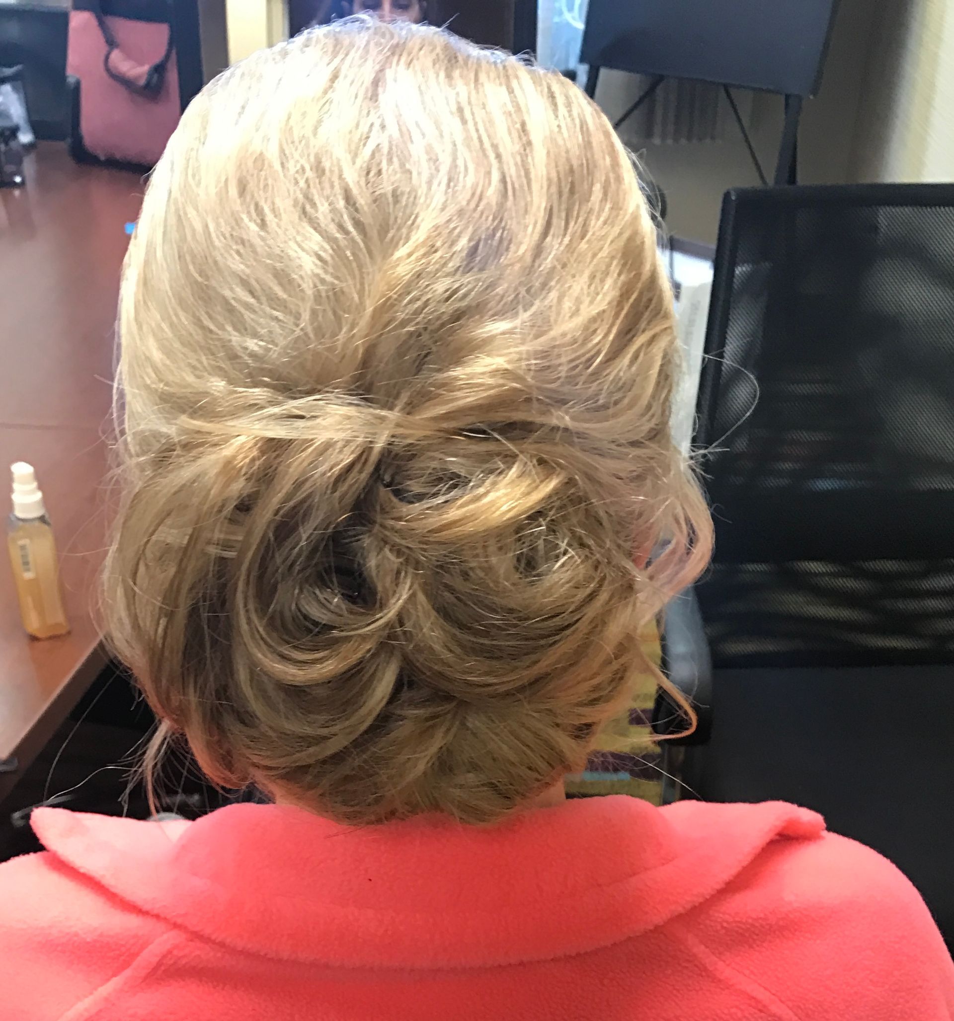 Woman with blonde hair styled in a low bun, wearing a pink collared shirt.