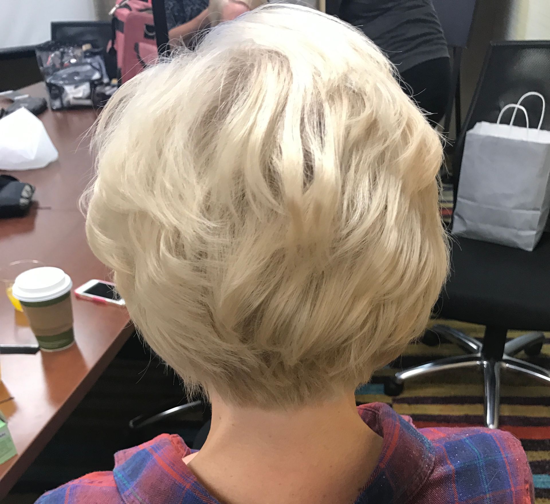 Back of a person's head with short, wavy, blonde hair. Sitting near a table with items.