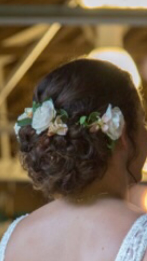 Woman with dark hair in an updo, decorated with white flowers and greenery.