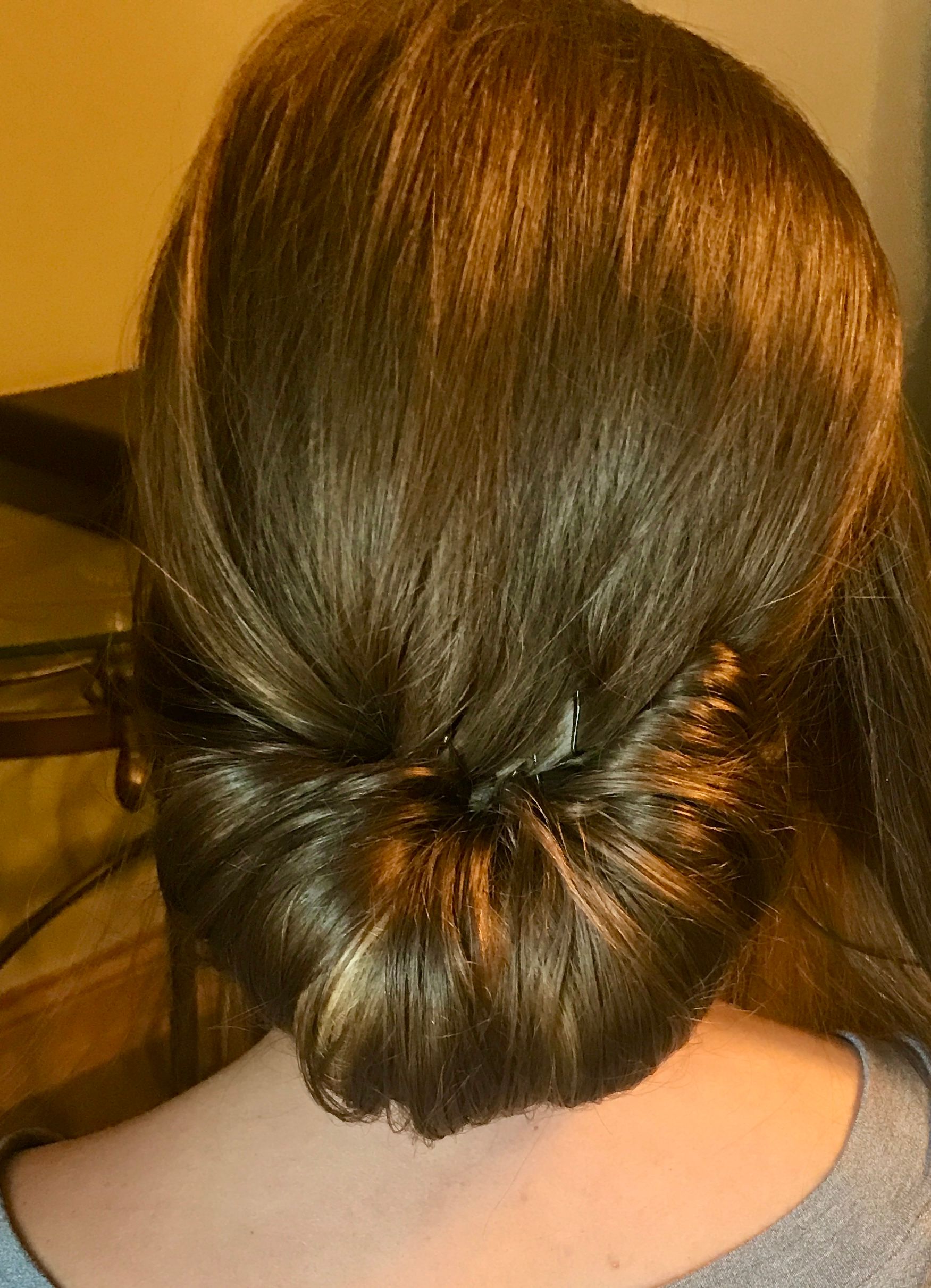 Woman with brown hair styled in a low bun, viewed from behind.