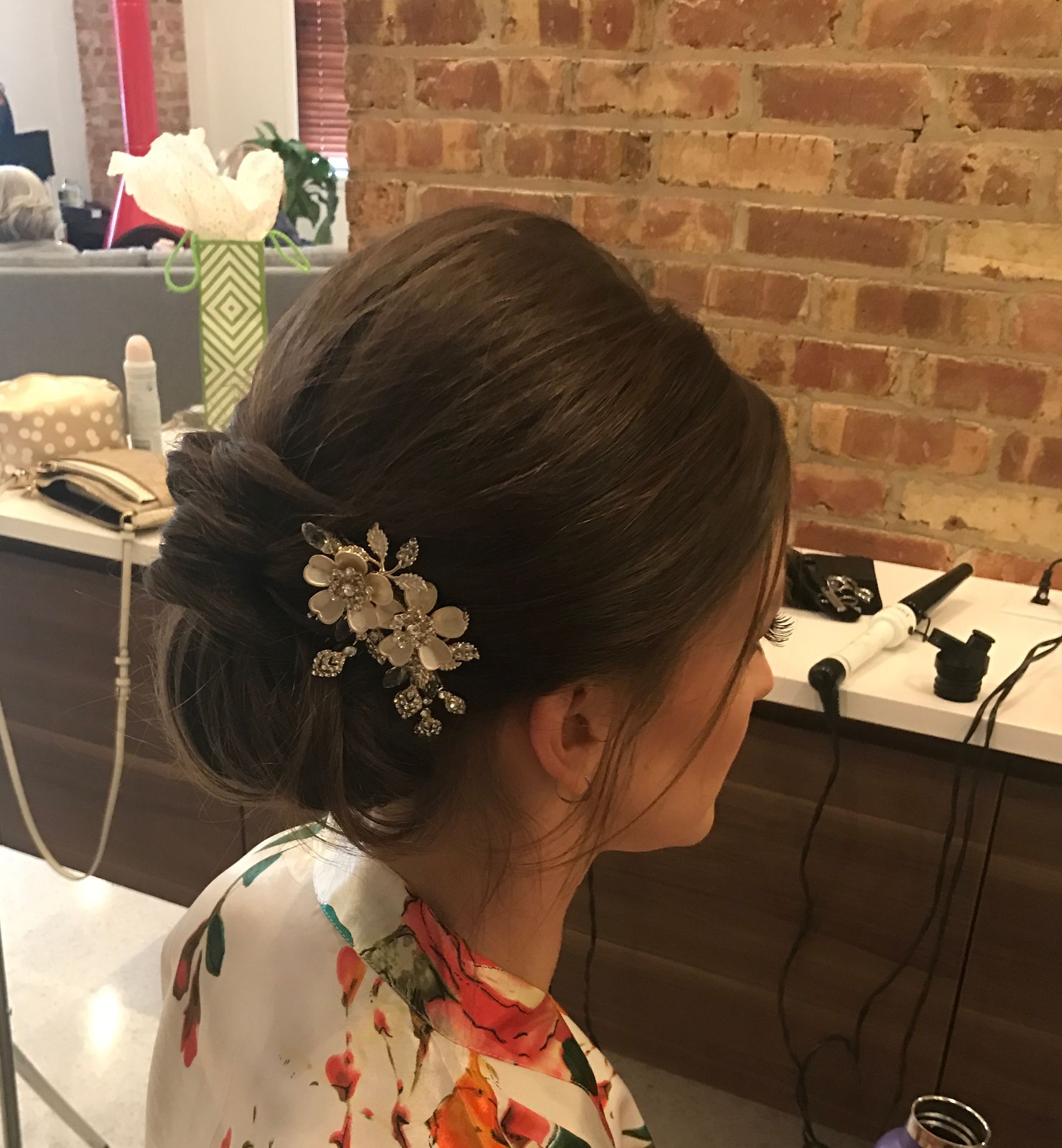 Woman with brown hair styled in a low bun, wearing a floral top, and adorned with a hair clip.