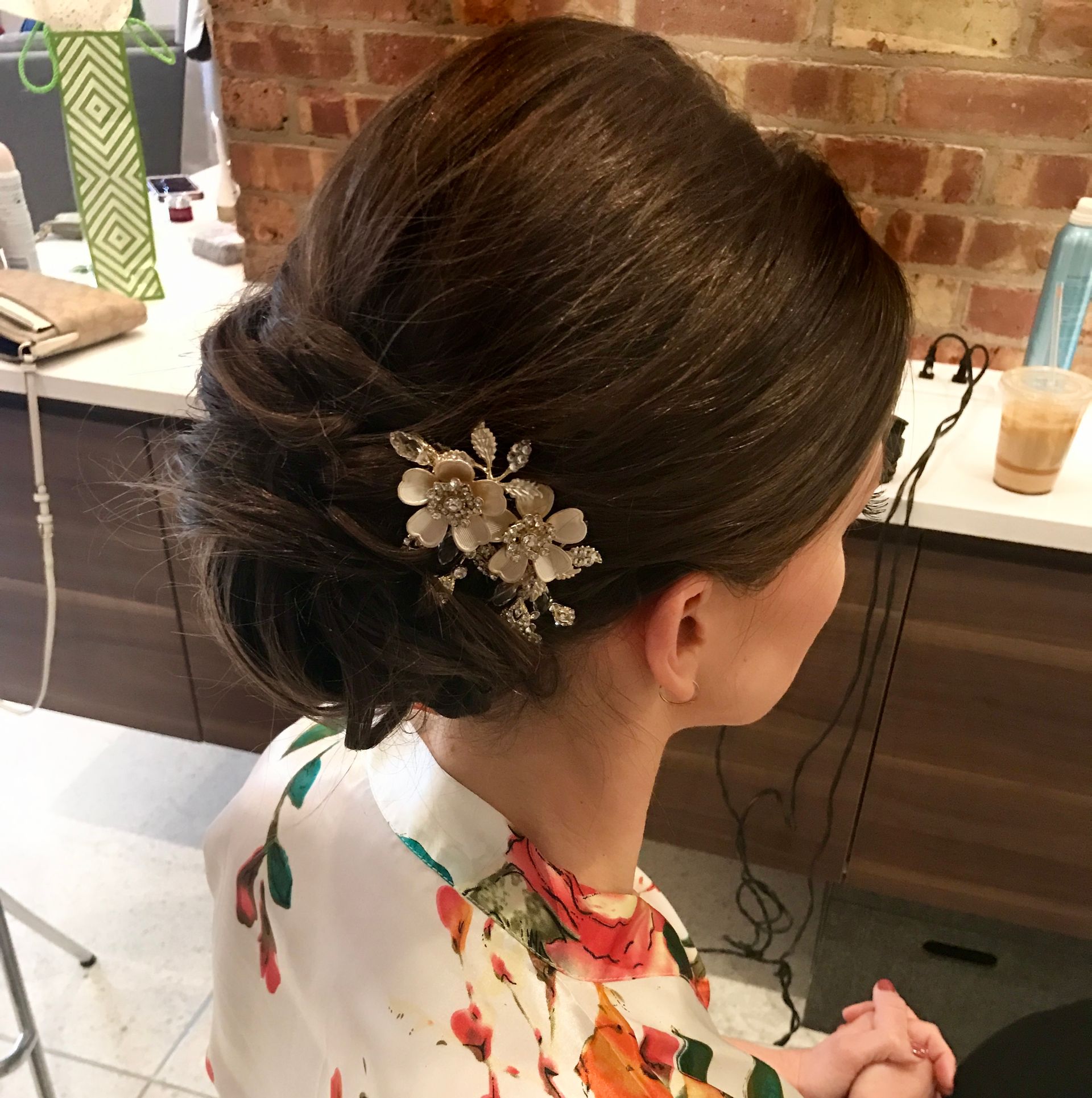 Woman with elegant updo hairstyle, decorated with a flower hairpiece. She is indoors.