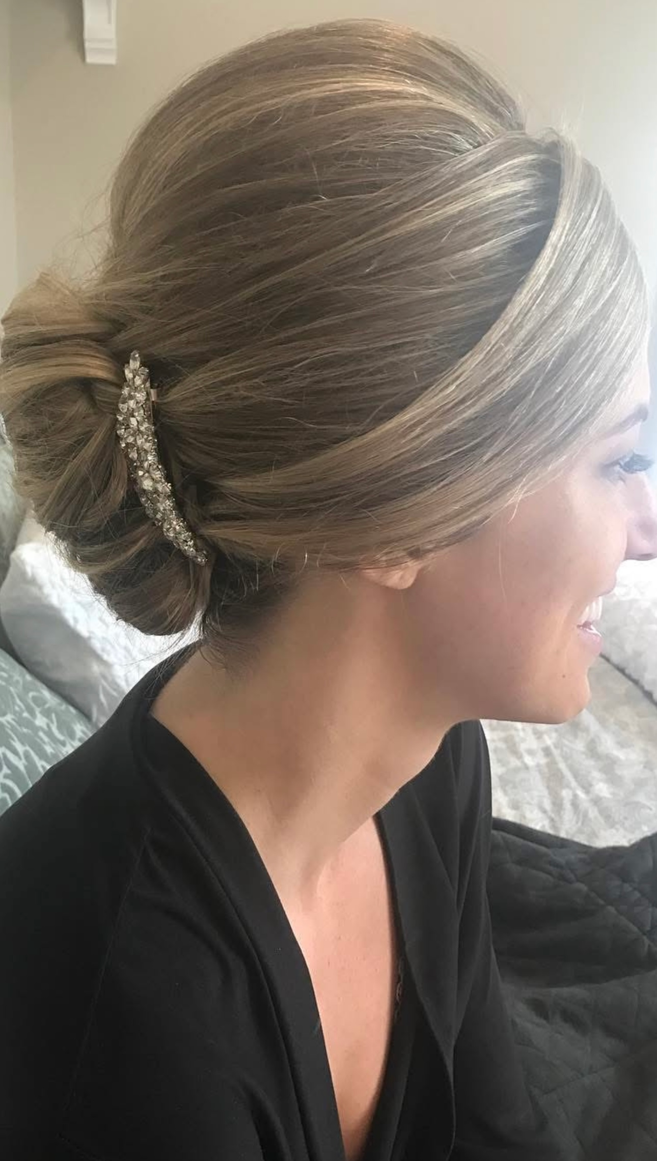 Woman with blonde updo hairstyle, wearing a dark robe, smiles.