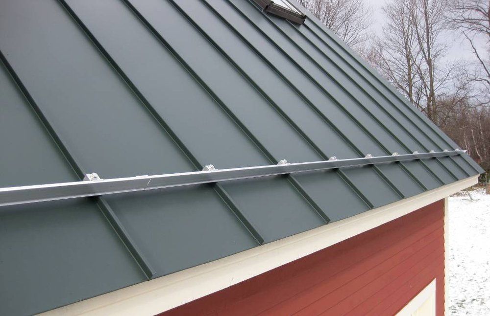 Brick building corner with a large glass window and metal roof under a partly cloudy sky.