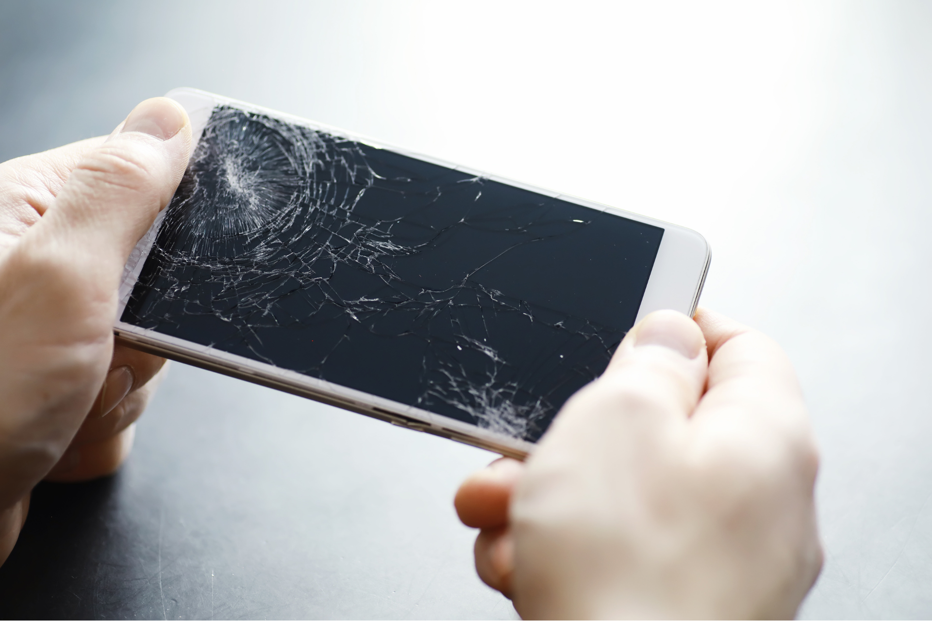 A person is holding a cell phone with a broken screen.