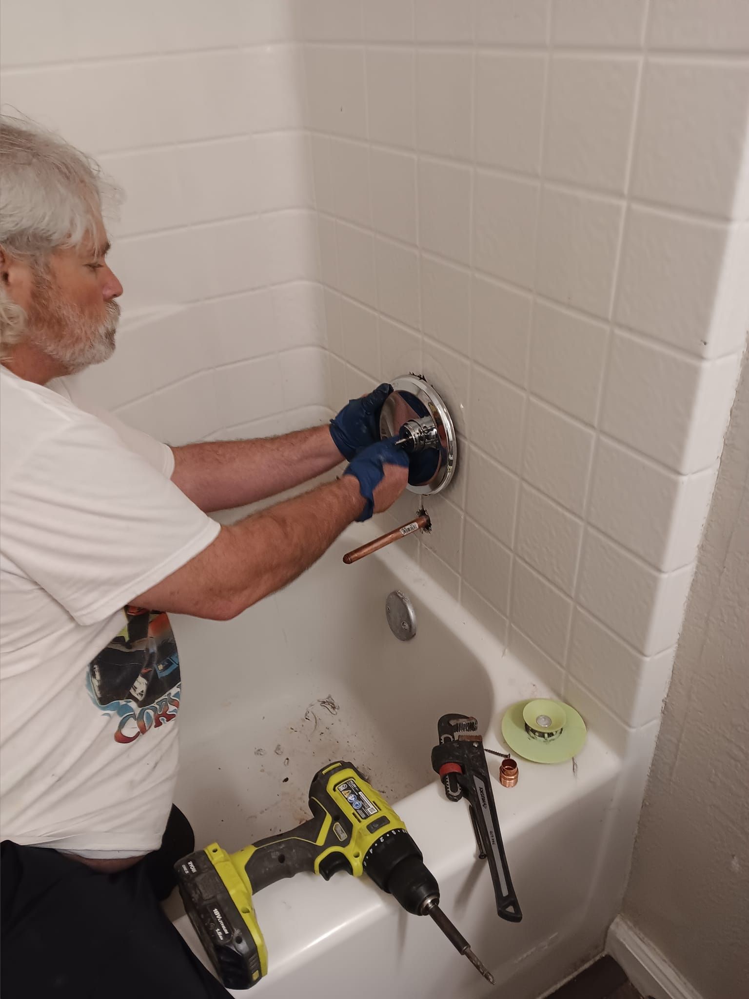 Person installing a shower fixture in a white-tiled bathtub, with tools on the tub rim