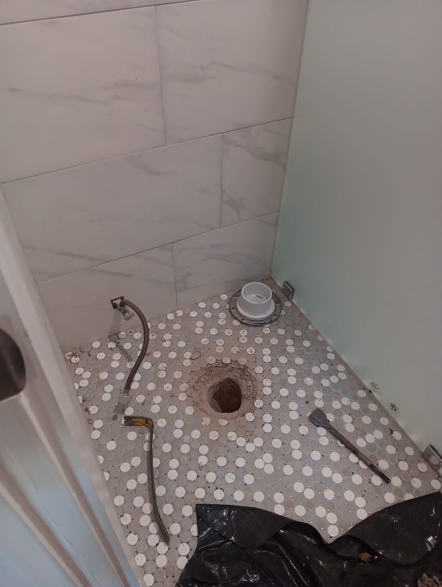Small bathroom renovation with exposed floor drain, loose pipes, tools, and tile debris.