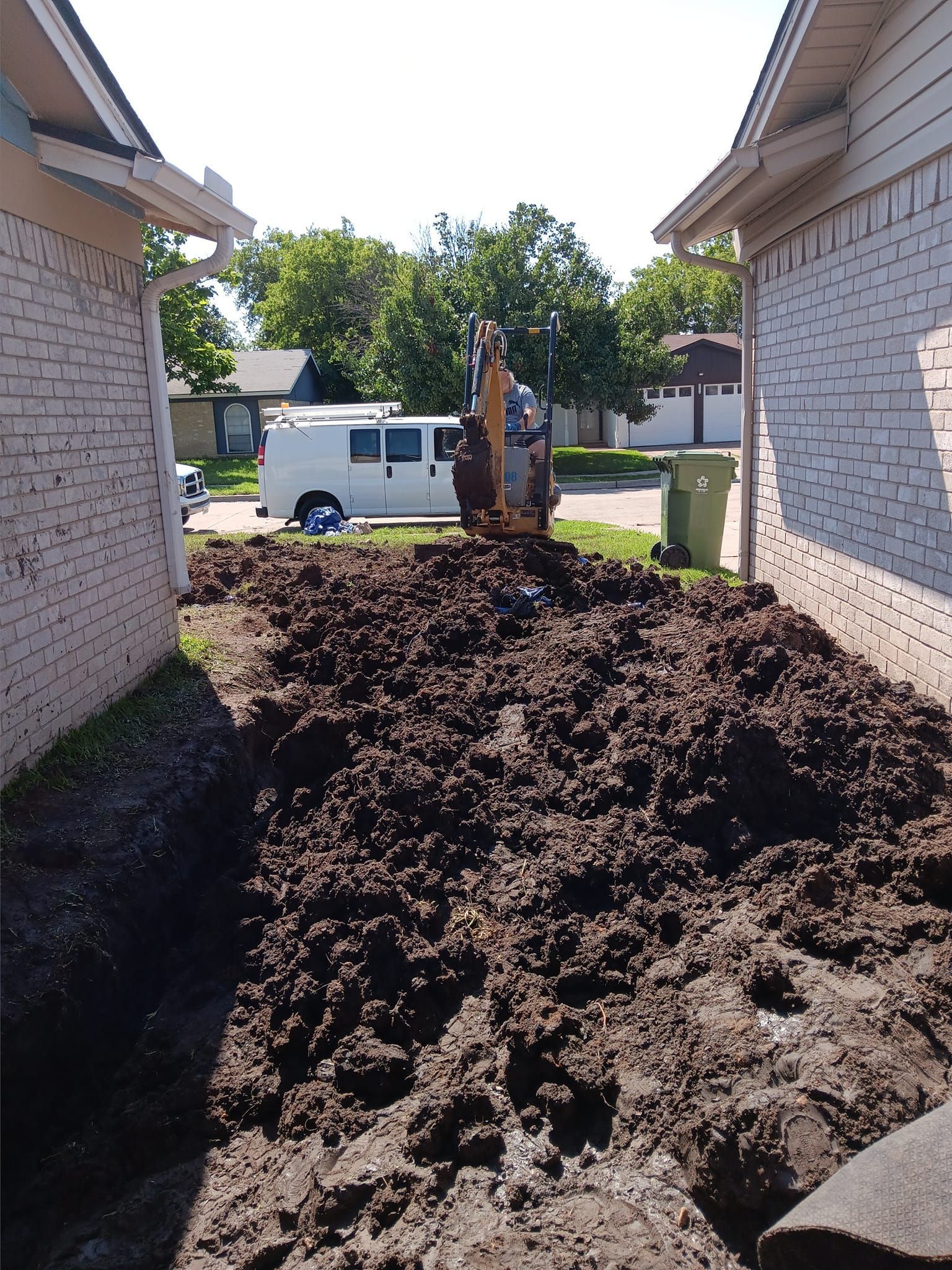 Backyard excavation with a small excavator and a large pile of dirt between two houses