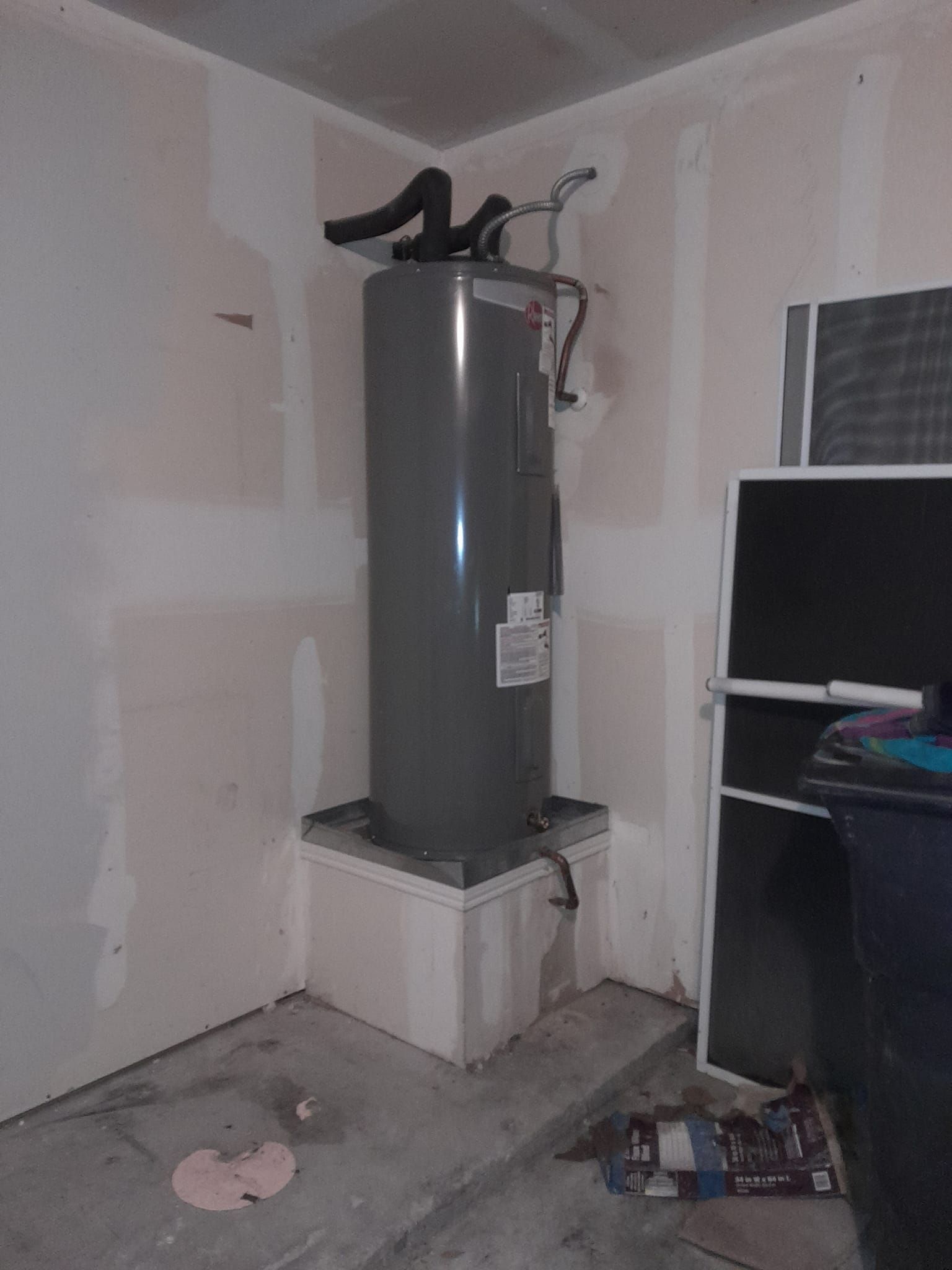 Water heater in unfinished utility room with white walls and concrete floor