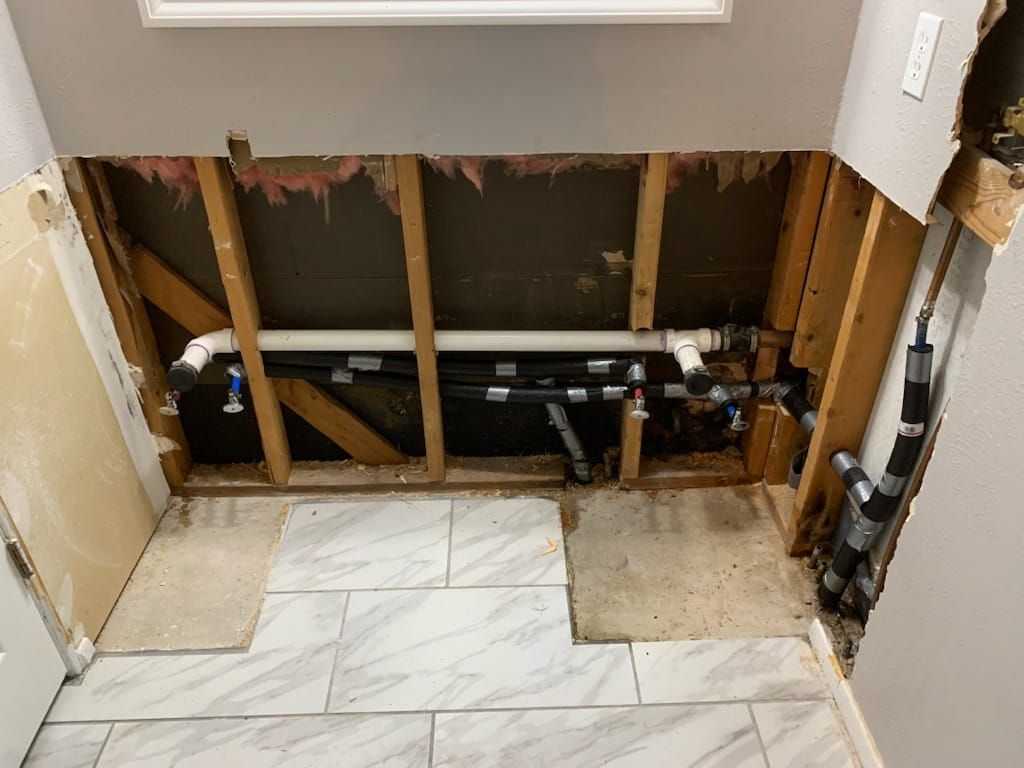 Bathroom vanity removed, exposing wall studs and plumbing above a tiled floor.