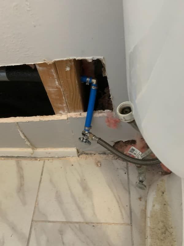 Blue water line and exposed plumbing by a wall opening above a tiled floor.