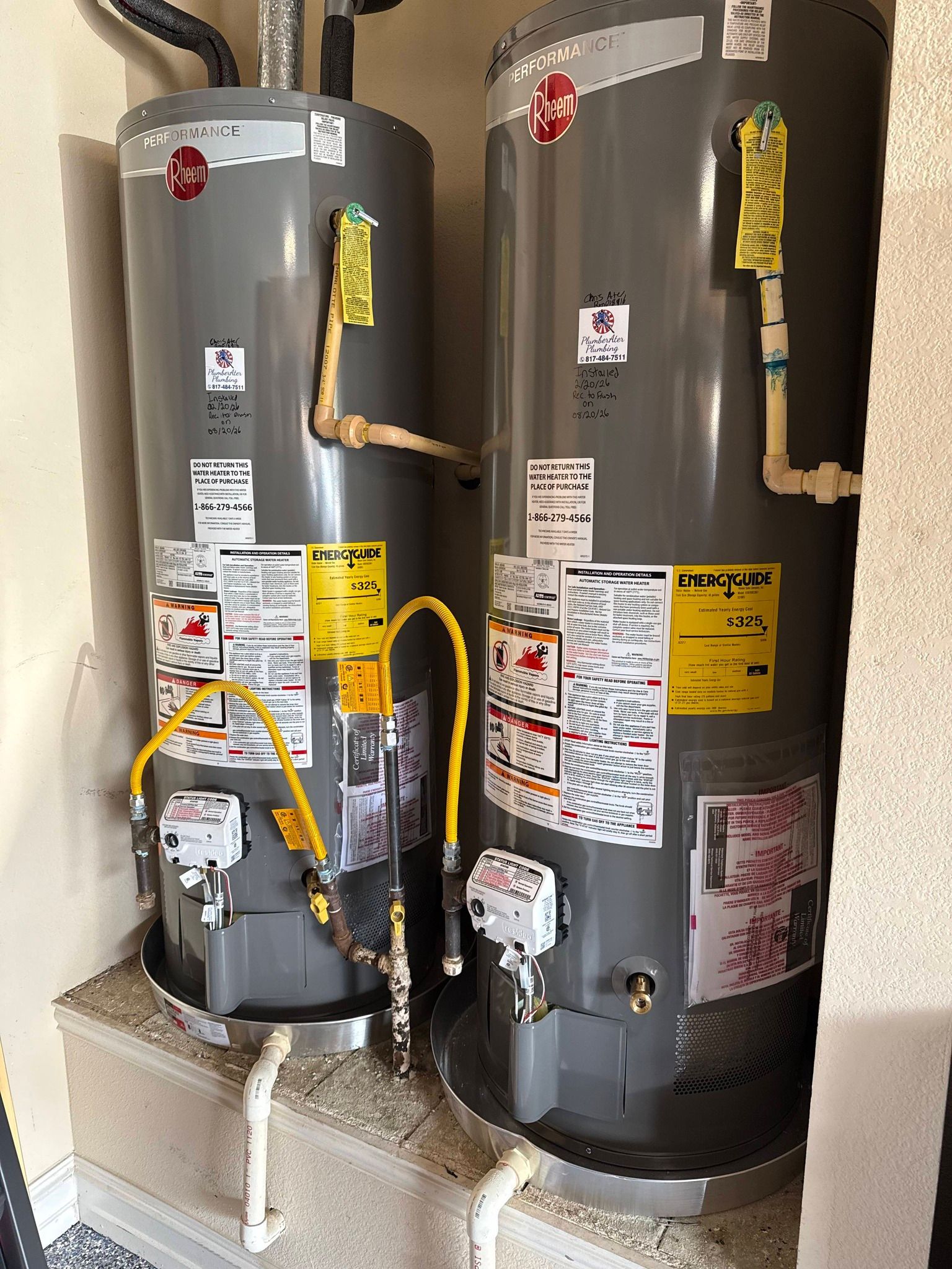 Two gray water heaters with pipes and warning labels in a utility room