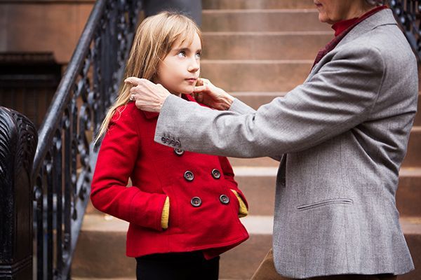 A woman is putting a red coat on a little girl.