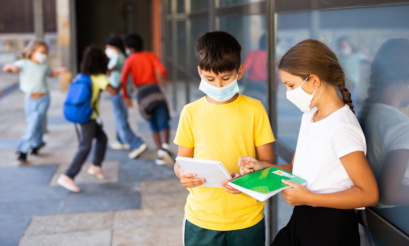 A boy and a girl wearing face masks with notebooks