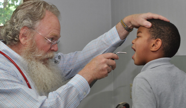 A man with a beard is examining a young boy