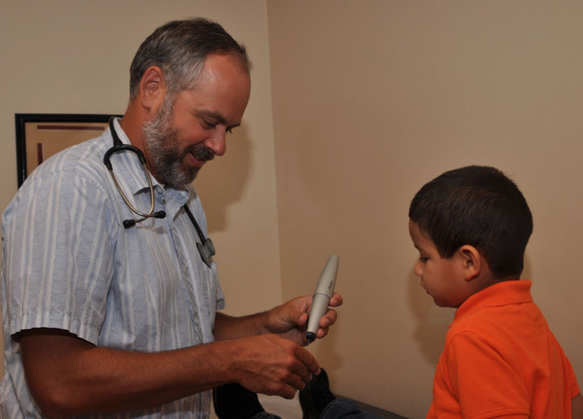 A doctor is talking to a young boy who is wearing an orange shirt