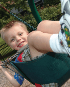 A young boy is sitting on a green swing and smiling