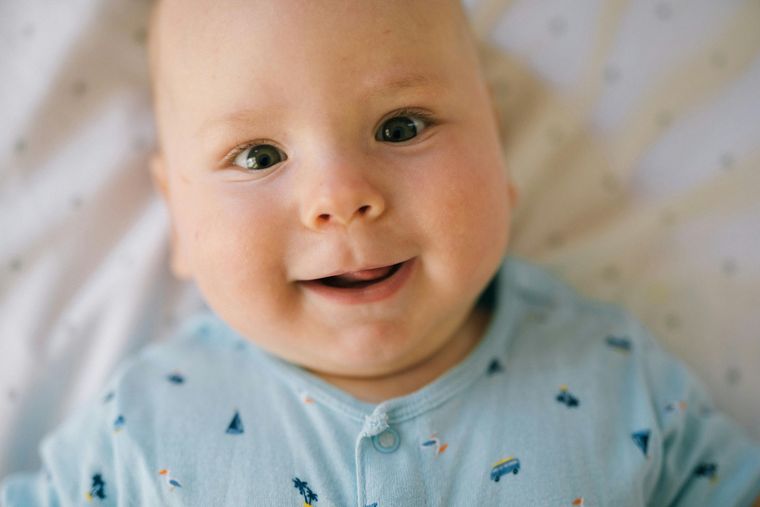 Smiling baby in blue pajamas looking directly at the viewer, lying in a crib.