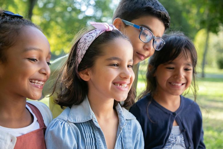 Group of diverse children smiling in a park, one wearing glasses.