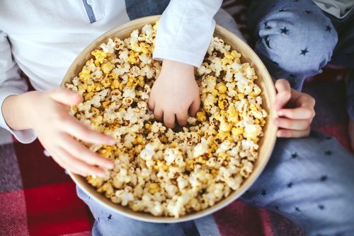 A child is reaching into a bowl of popcorn.
