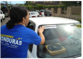 Putting bumper stickers on cars to promote the Transformemos Honduras alliance in 2009