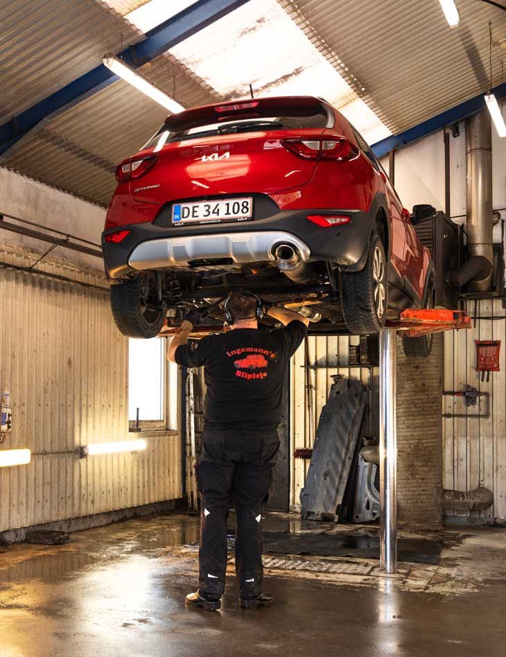 Mekaniker arbejder under en rød Kia SUV på en lift i en garage.