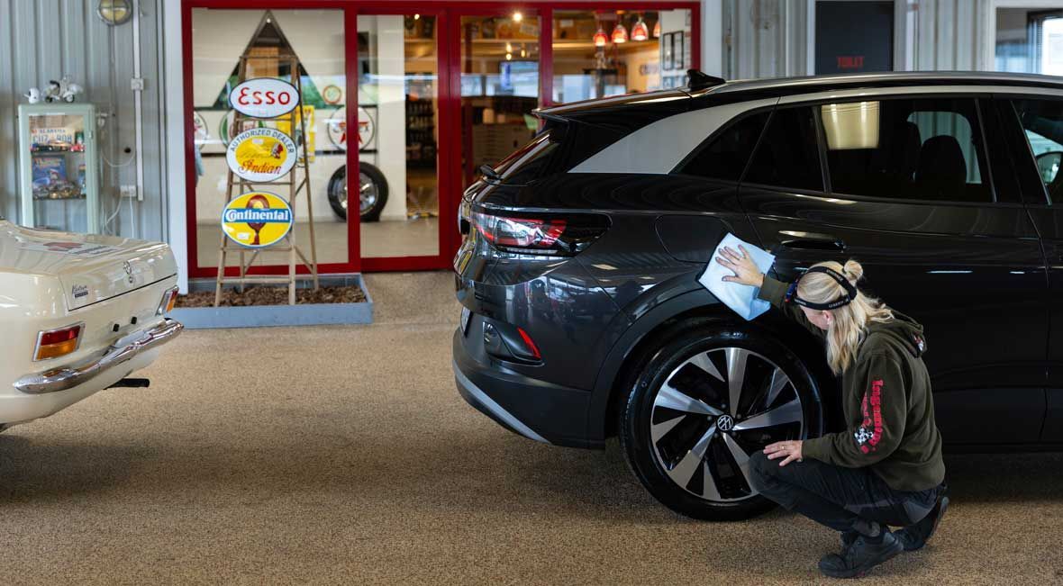 Person undersøger dæk på en mørkegrå SUV i en butik med en veteranbil og et skilt med en tankstation.