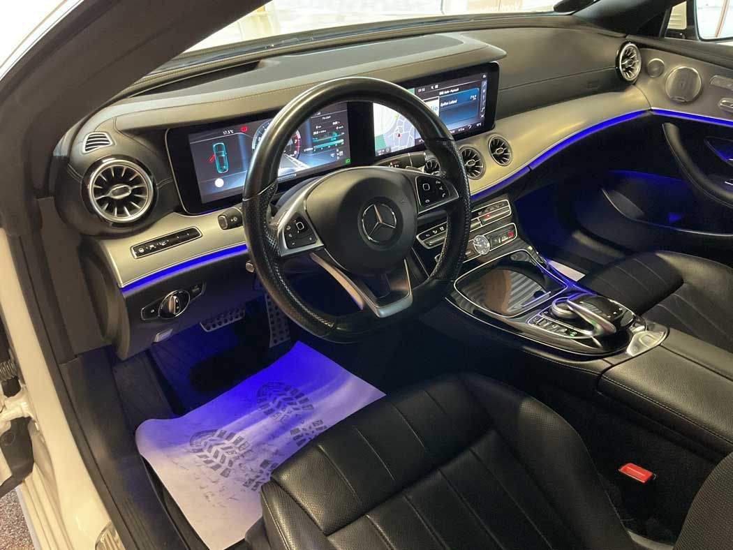 Interiør i en Mercedes Benz. Rat, dobbelte displays, sorte lædersæder og blå ambientebelysning.