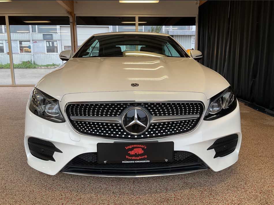 Hvid Mercedes-Benz bil, set forfra, parkeret indendørs med et forhandlermærke på kofangeren.