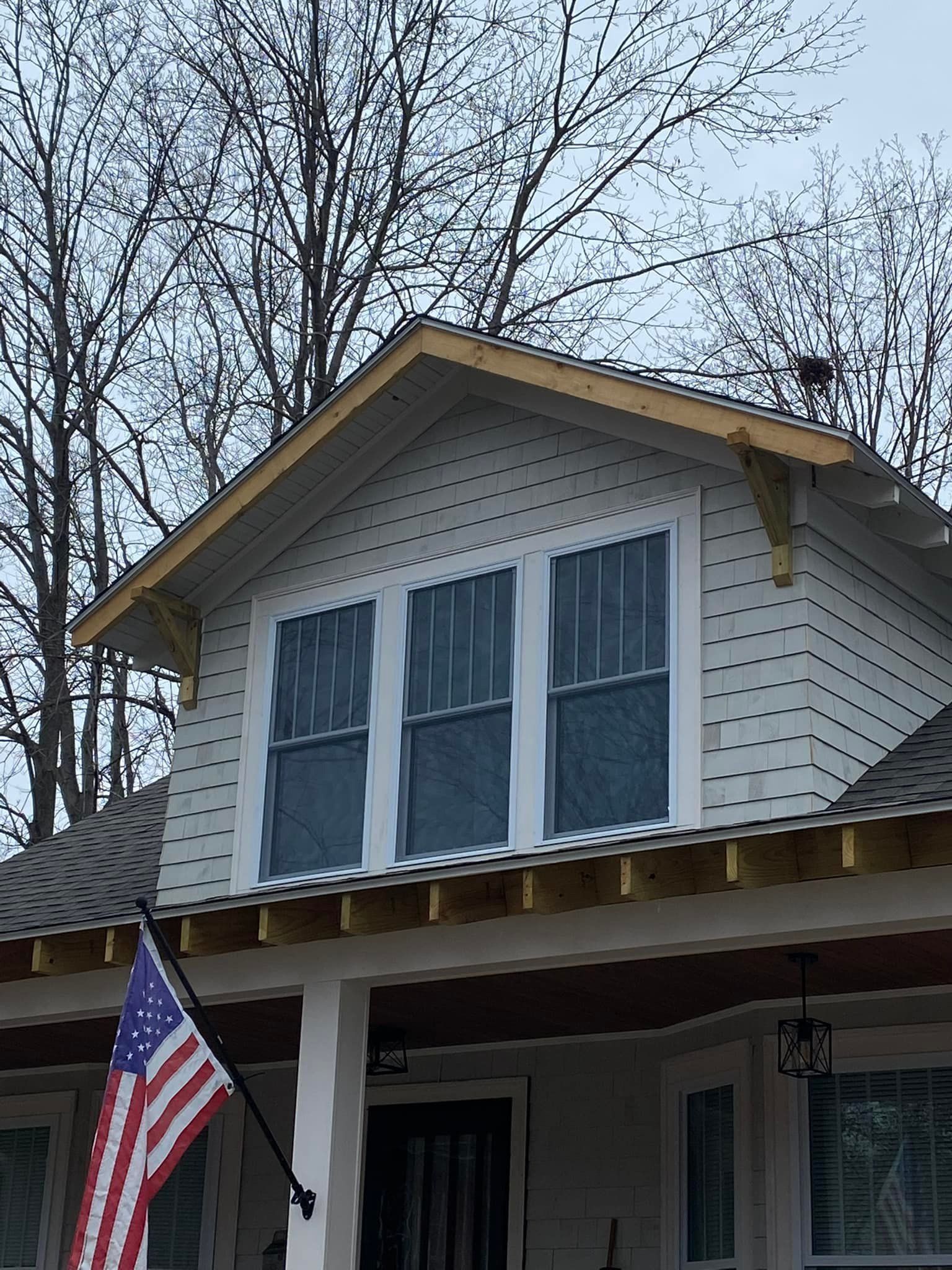 A house with a flag on the porch and a bird on the roof.