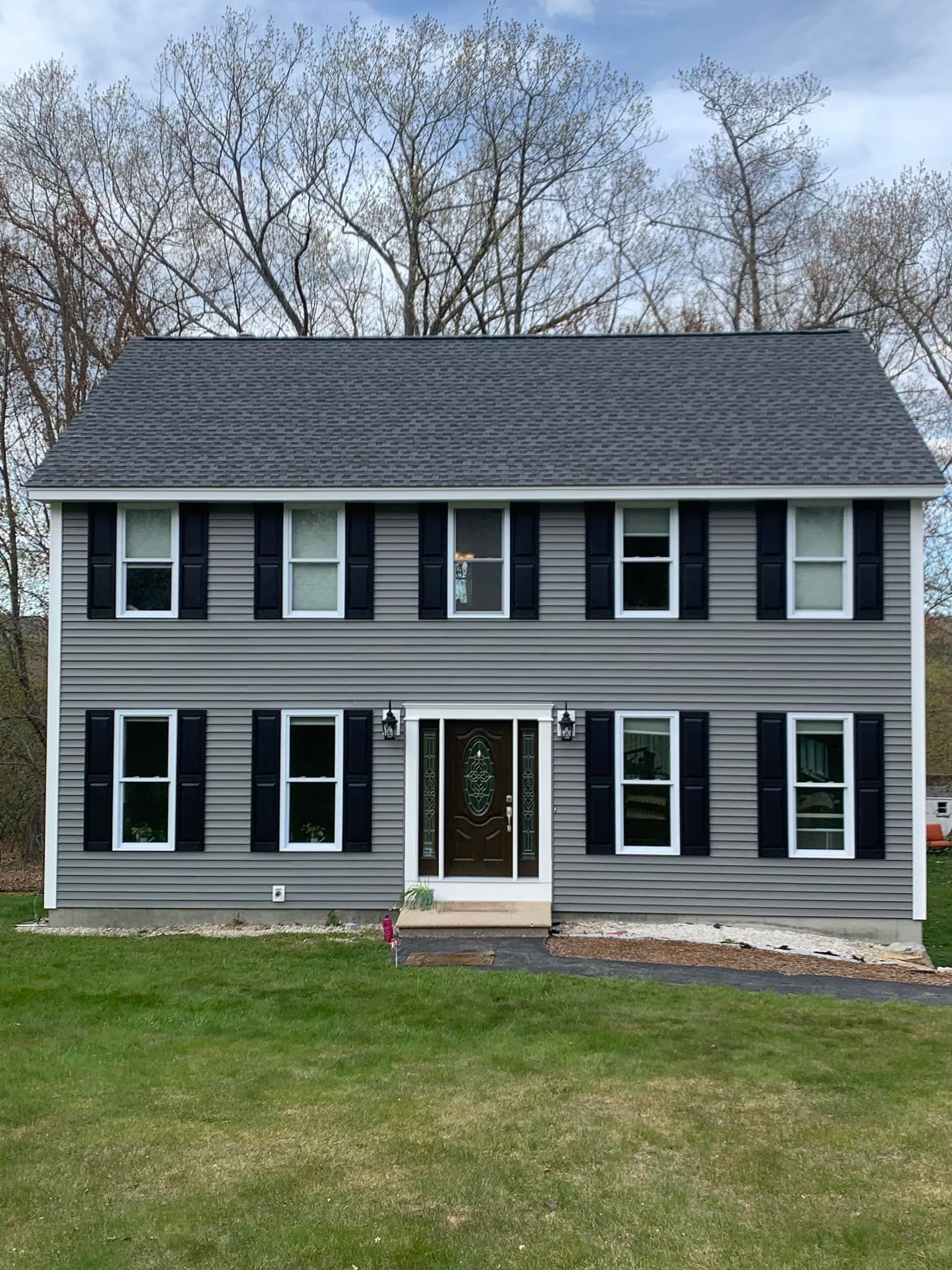 A large gray house with black shutters is sitting on top of a lush green field.